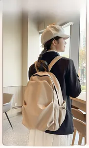 Beige nylon backpack detail featuring side drawstring pockets on a model in a cafe