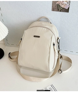 Detailed view of cream nylon backpack with multiple zipper pockets and metal brand logo