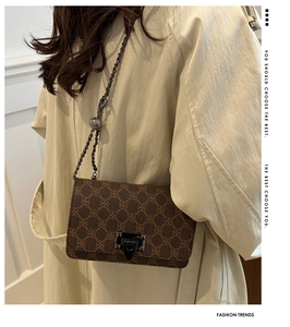 Close-up of brown monogram crossbody bag on a beige trench coat with chain strap detail