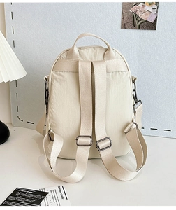 Detail view of beige backpack back with adjustable straps and grey metal side hooks