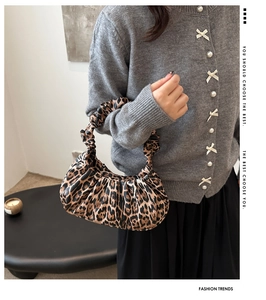 Detailed view of pleated crescent handbag with leopard print and ruffled wrist strap