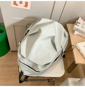 Minimalist light gray water-resistant backpack on a white metal chair for school use