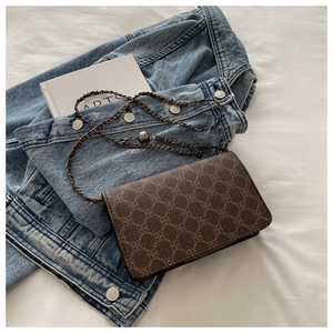 Detail view of vintage brown monogrammed shoulder bag with leather chain strap on denim