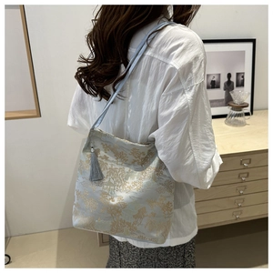 Detail of light blue satin tote bag featuring gold oriental landscape embroidery and grey tassel
