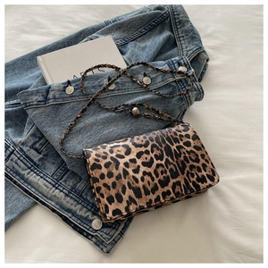 Detailed shot of leopard print crossbody bag with metal chain strap on textured fabric