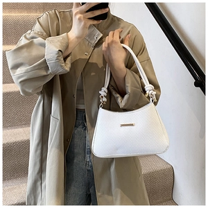 Detail of white quilted handbag featuring a golden logo and knotted shoulder strap detail