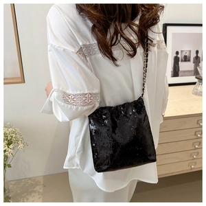 Close-up of black sequined crossbody bag with golden chain strap on a stylish model