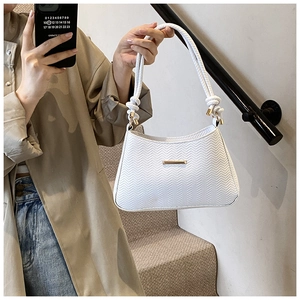 Detail of white quilted handbag with braided rope handle and golden metal accents