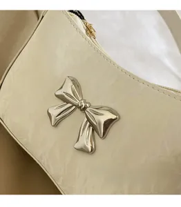 Close-up of a silver 3D bow hardware detail on a creamy white leather shoulder bag