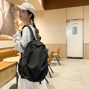 Close-up of a large black minimalist backpack worn by a student in a cozy cafe setting