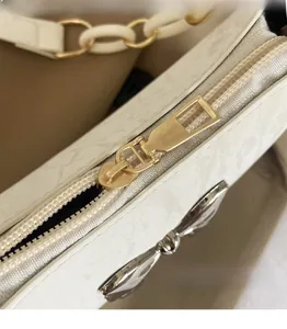 Detail of white embossed leather bag featuring gold hardware zipper and bow charm