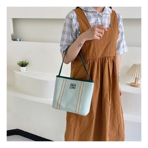 Detailed close-up of mint green canvas bucket bag featuring orange stripes and MIDU logo