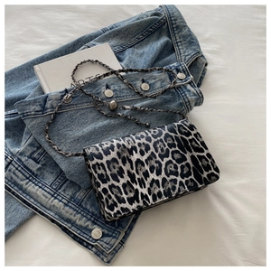 Detail of leopard print crossbody bag with woven chain strap on blue denim and white sheet