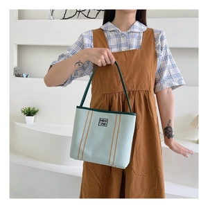 Close-up of light blue canvas tote bag with brown stripes and green rounded handles