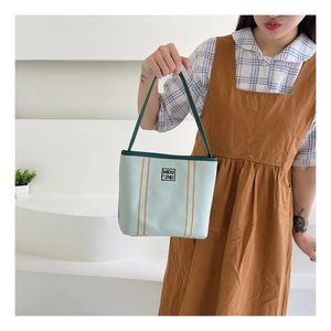 Detail of mint green canvas handbag showing vertical orange stripes and brand logo