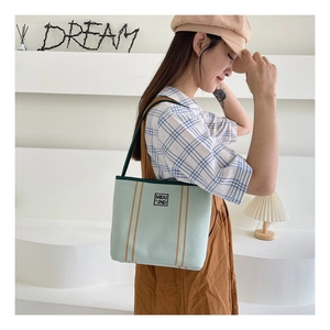 Detail of light green canvas tote bag with brown stripes and MIDU logo on model
