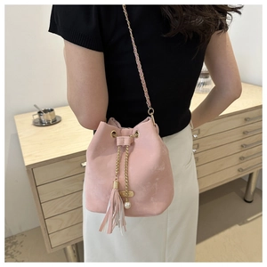 Pink suede bucket bag with chain strap and pearl tassel detail shown on shoulder