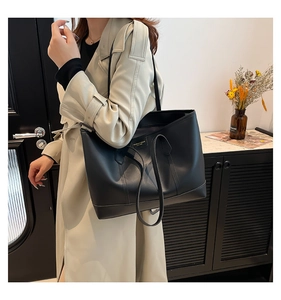 Detail of minimalist black leather tote bag with logo plate worn on shoulder with trench coat