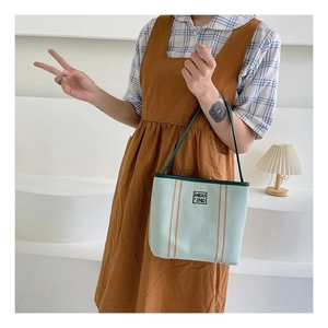 Detail view of light green canvas tote bag with orange stripes and shoulder strap design