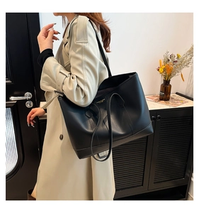 Side view of a black matte leather tote bag worn by a model in a minimalist interior
