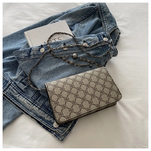 Close-up of vintage chain crossbody bag with clover pattern over denim and books