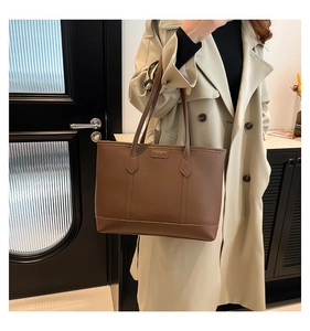 Deep brown leather tote bag detail with vertical stitching and metal logo plate