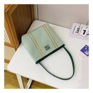 Detail view of mint green canvas bucket bag with dark green handles in a home setting