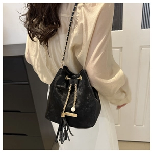 Detail view of black bucket bag featuring leather fringe, pearl charm, and chain strap
