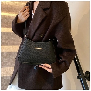 Detail of black leather shoulder bag featuring herringbone texture and gold metal bar