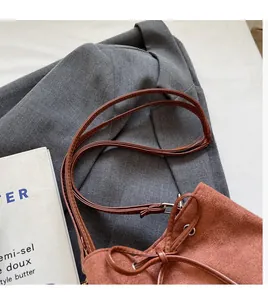 Detail of brown suede bucket bag with drawstring bow on a grey blazer jacket