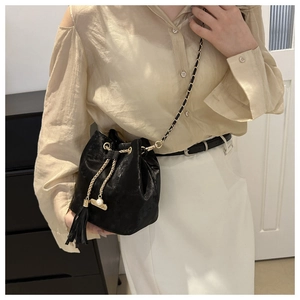 Close-up of black bucket bag featuring gold chain strap, tassels and pearl charm detail