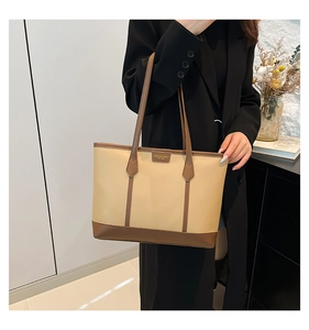 Detail of a chic tote bag featuring beige fabric with brown leather straps and trim