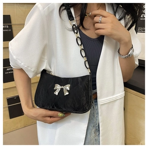 Detail of black crescent shoulder bag with silver bow accent and chain strap worn by a model