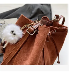 Detail of brown suede bucket bag with drawstring closure and fuzzy eye charm
