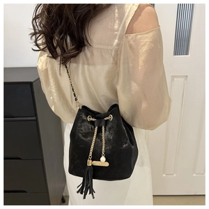Detail of black drawstring bucket bag with gold tassel, pearl charm, and woven chain strap