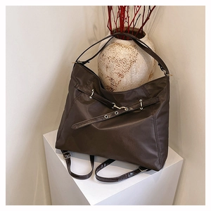 Detail view of dark brown tote bag on white stand with sleek metal buckles and nylon texture