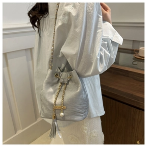 Close-up of a silver bucket bag with gold chain strap and pearl tassel detail on model