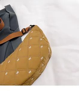 Detail der gelben gesteppten Halbmondtasche mit weißer Schleifenstickerei und Gurt