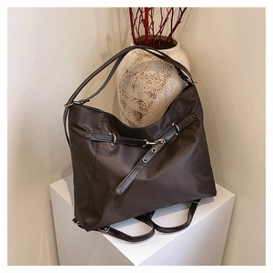Detail of chocolate brown nylon tote bag showing leather straps and metallic buckle on white stand