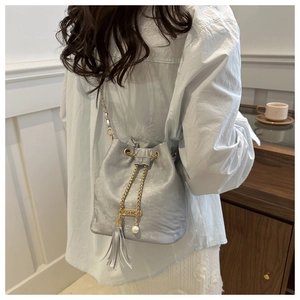 Close-up of silver bucket bag with gold chain strap, pearl detail, and tassel charm
