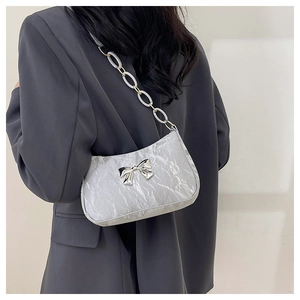 Detail of silver metallic shoulder bag with bow buckle and resin chain strap on model