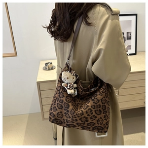 Detail view of a large leopard print bucket bag with a plush decorative charm