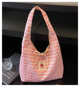 Detail of checkered canvas bag featuring a red tomato logo patch and decorative bow