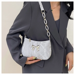 Detail of silver metallic underarm bag with bow ornament and stylish chain strap