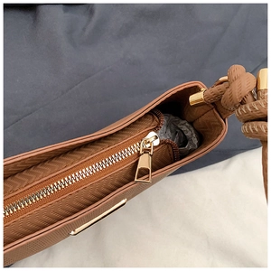Detail of golden zipper closure and braided shoulder strap on brown embossed bag