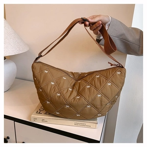 Detail einer braunen Stepptasche mit weißen Bogentickereien und Gurtband-Schultergurt