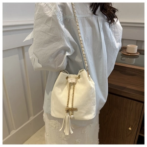 Detailed view of beige velvet bucket bag with gold chain and pearl tassel detail