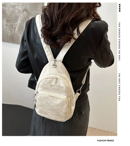Detail of white wrinkled leather backpack with silver zippers worn by model for daily commute