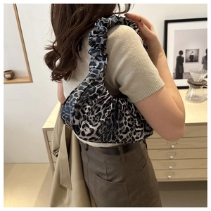 Detail of blue leopard print crescent bag with ruffled strap worn as an underarm bag