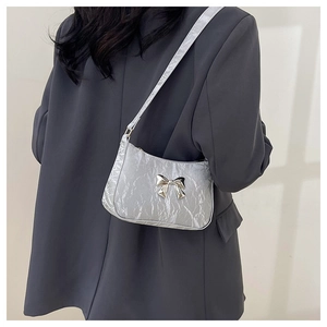 Detailed side view of silver ruched baguette bag with a metal bow on a dark grey blazer